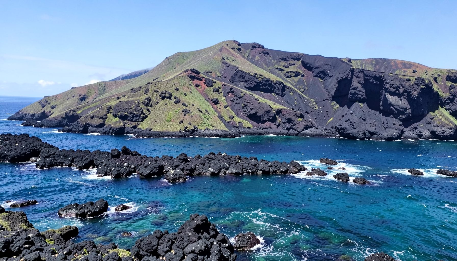Dramatic volcanic coastline of the Galápagos Islands with dark lava rock, turquoise water, and a clear sky, evoking the archipelago's unique natural beauty