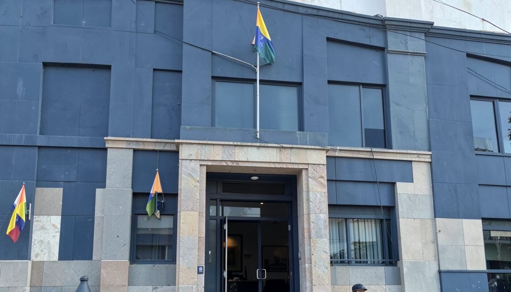 A calm official-looking building facade in muted navy blue and stone tones, with a subtle Ecuadorian flag detail, conveying a formal diplomatic mood